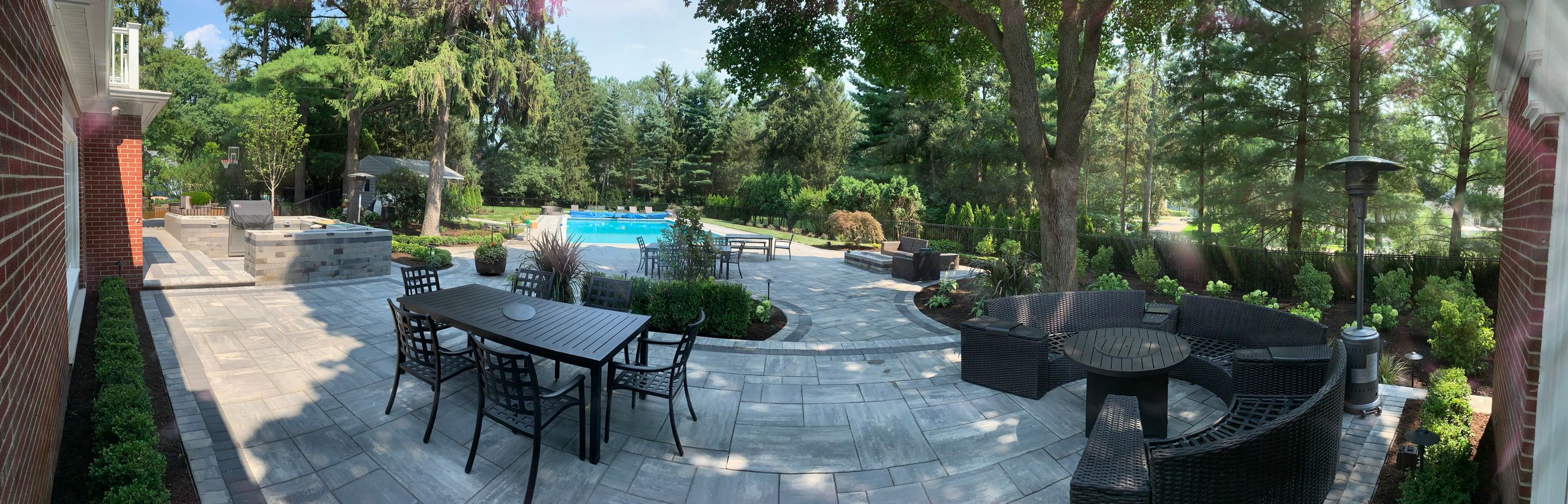 Paver patio with outdoor kitchen, paver walkway and pool surround, planters with flowers, and boxwood hedges and mulched beds.